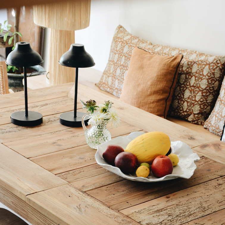 Houten tafel met decoratieve witte fruitschaal en twee zwarte tafellampen in een gezellige ruimte