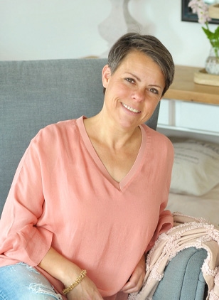 Lachende vrouw in roze blouse zittend op grijze bank in lichte kamer