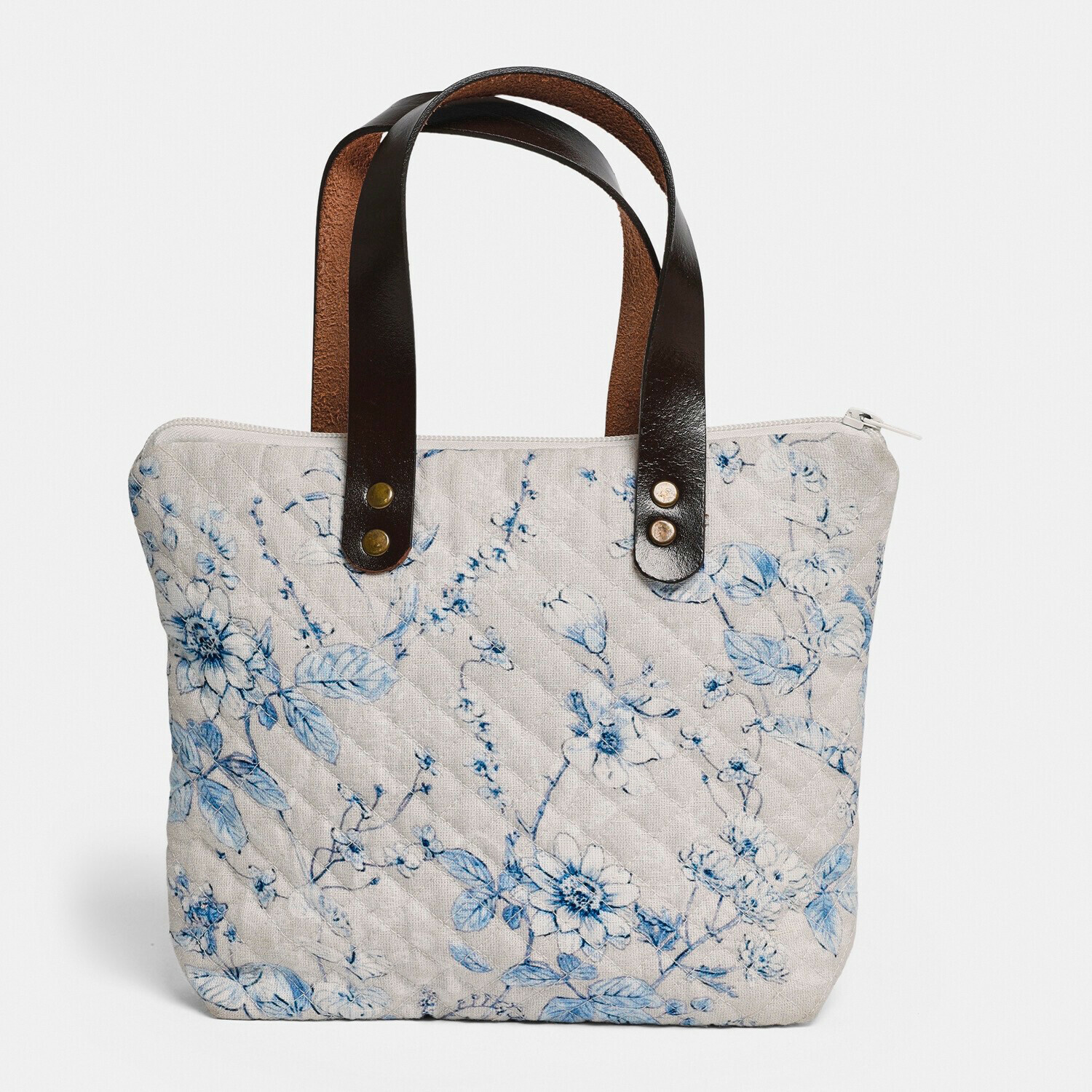 Beige gewatteerde tas met blauw bloemenpatroon en zwarte leren handvatten, modieuze accessoire