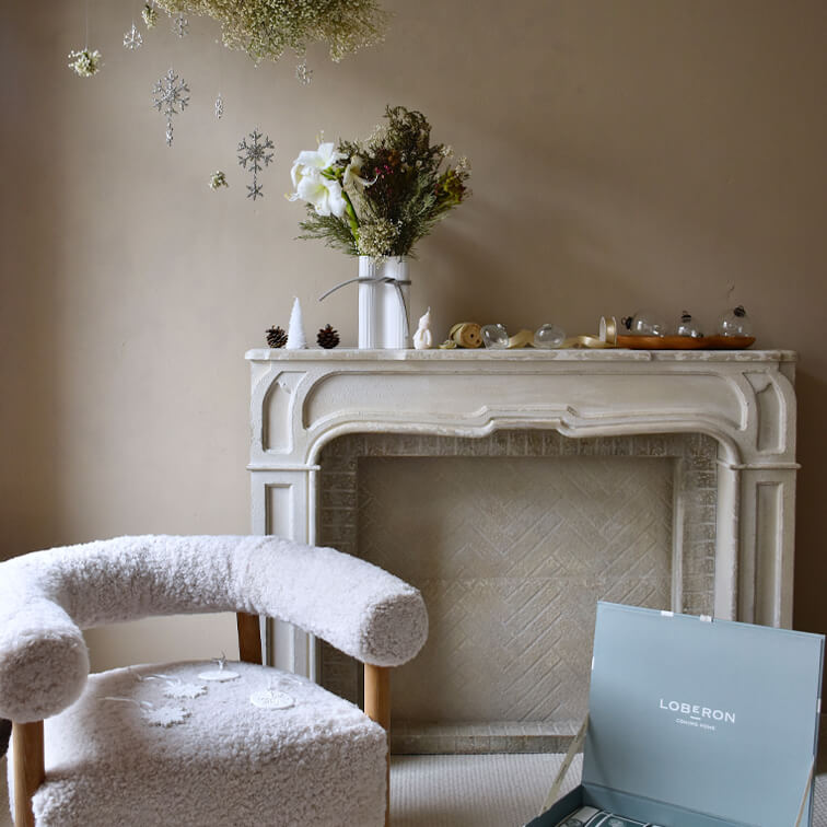 Knus witte stoel met zachte bekleding naast een decoratieve open haard en hangende sneeuwvlokken