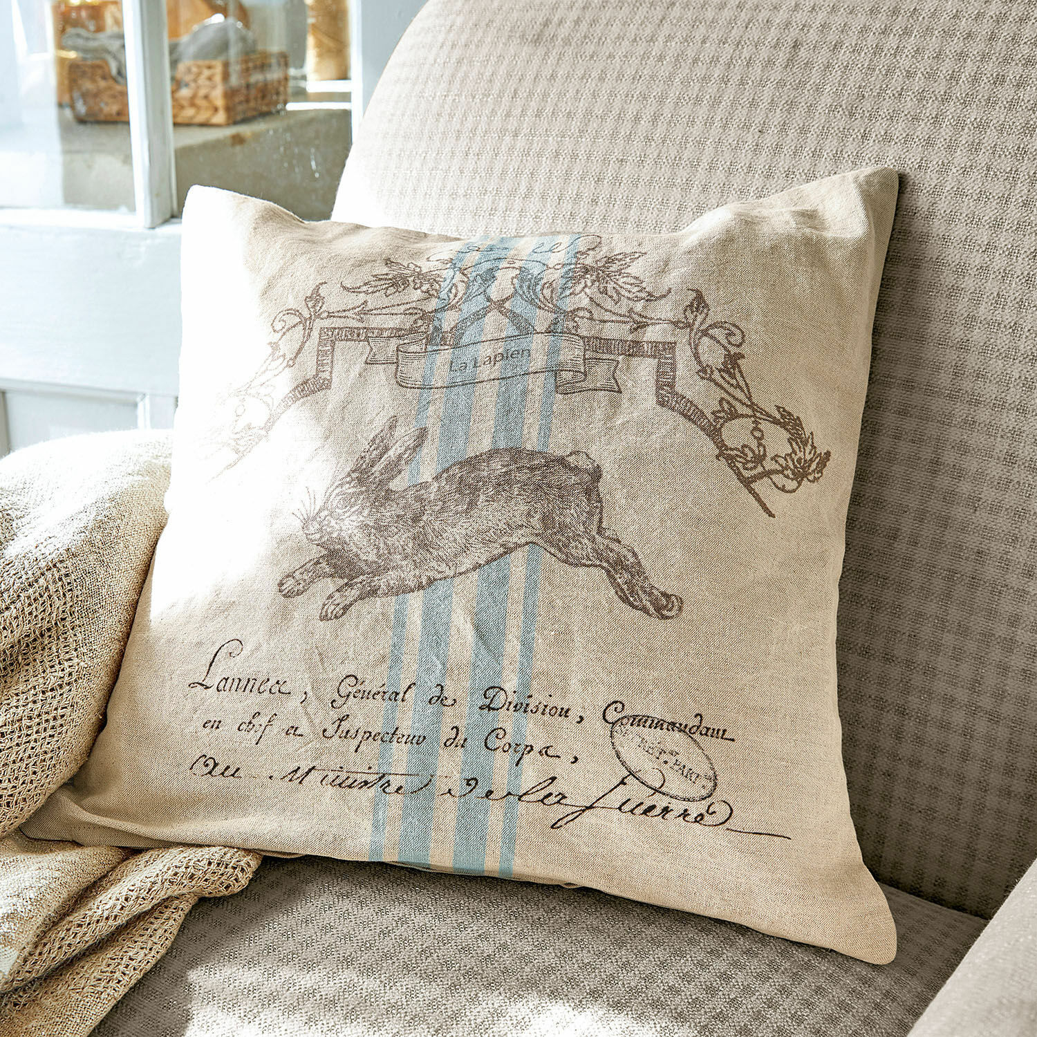 Kussenhoes La Lapin Beige linnen kussen met haasprint en blauwe strepen op grijze bank, woondecoratie