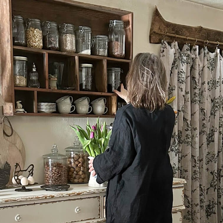 Vrouw in zwarte jurk pakt pot van houten plank met keukengerei en tulpen in de hand