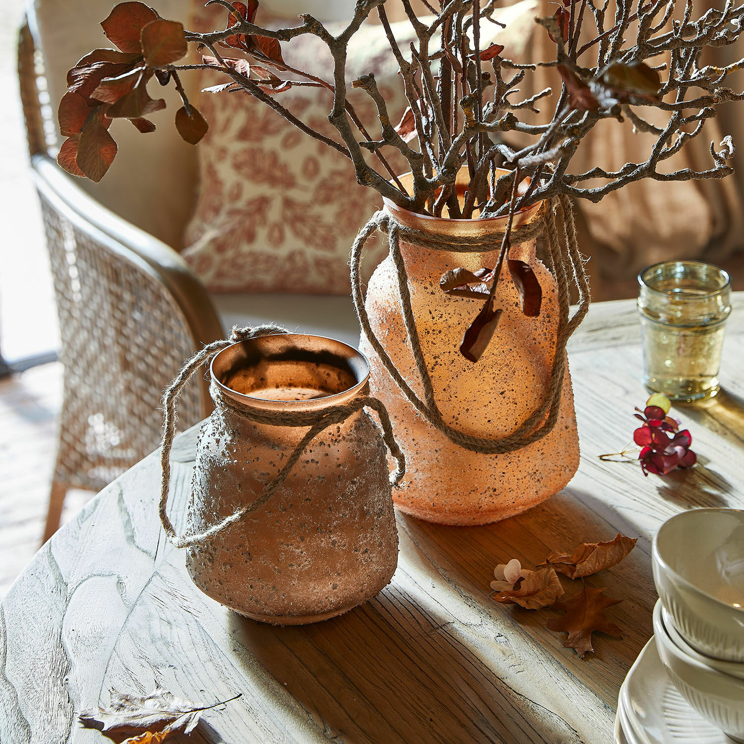 Twee decoratieve vazen van mat oranje glas met touwen op een houten tafel in een lichte woonkamer