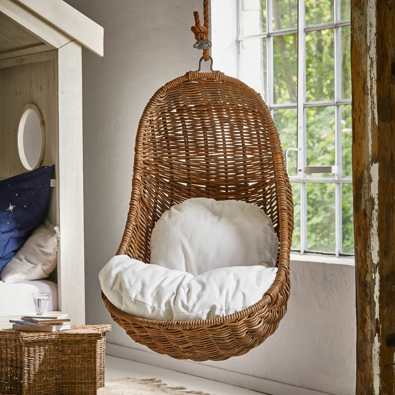 Kinderhangstoel Twinkla Hangstoel van rotan met wit kussen in lichte, natuurlijke kamer met groot raam