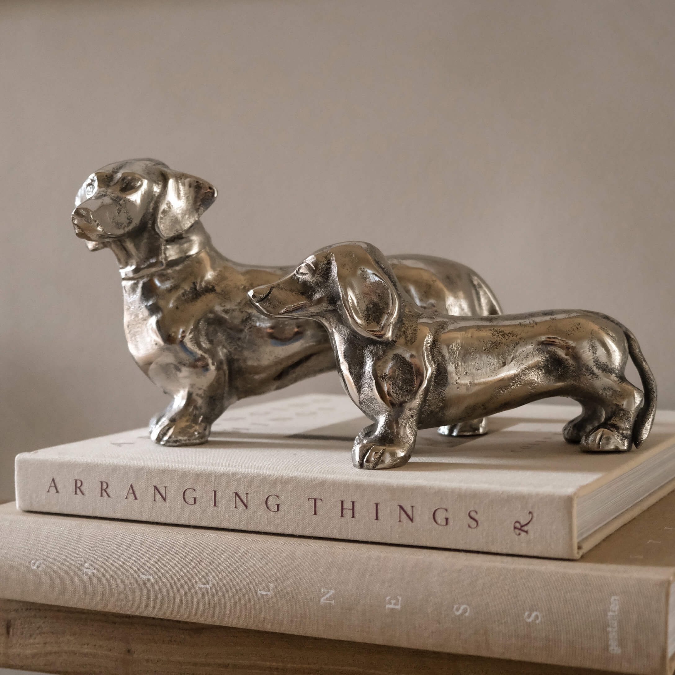 Twee zilverkleurige metalen teckelbeeldjes op een stapel boeken als interieurdecoratie