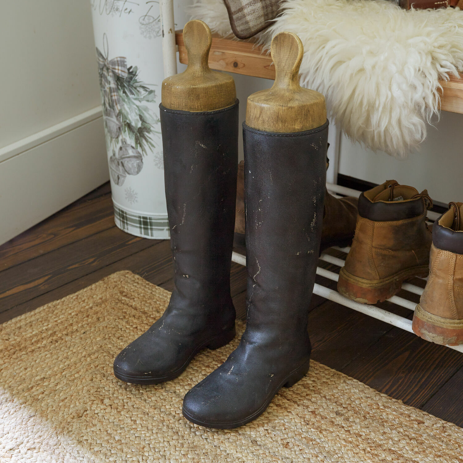 Zwarte leren hoge laarzen met houten schoenspanners op een vloerkleed in de hal