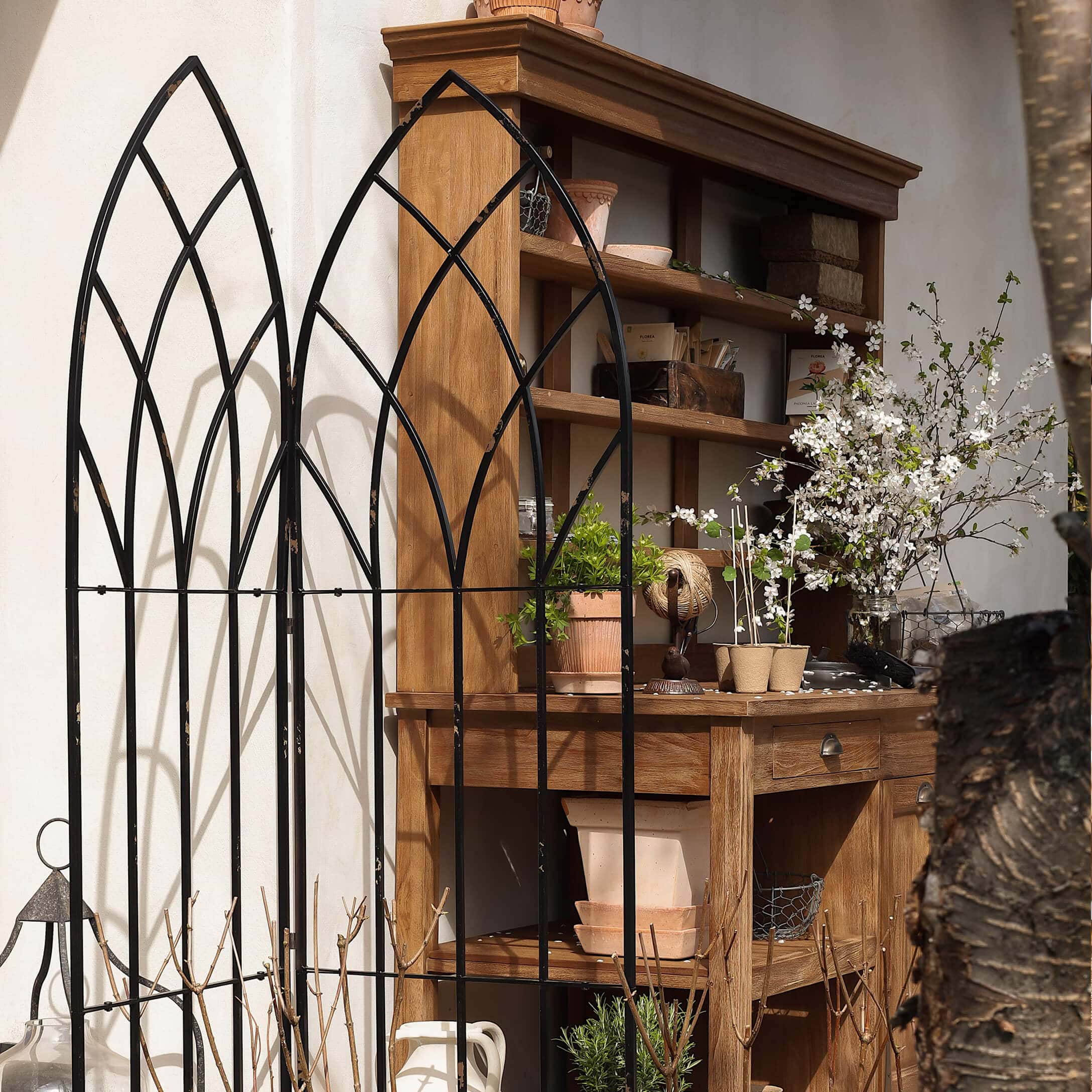 Zwart metalen tuinrek met boogvormig patroon voor houten kast met bloempotten en bloemen