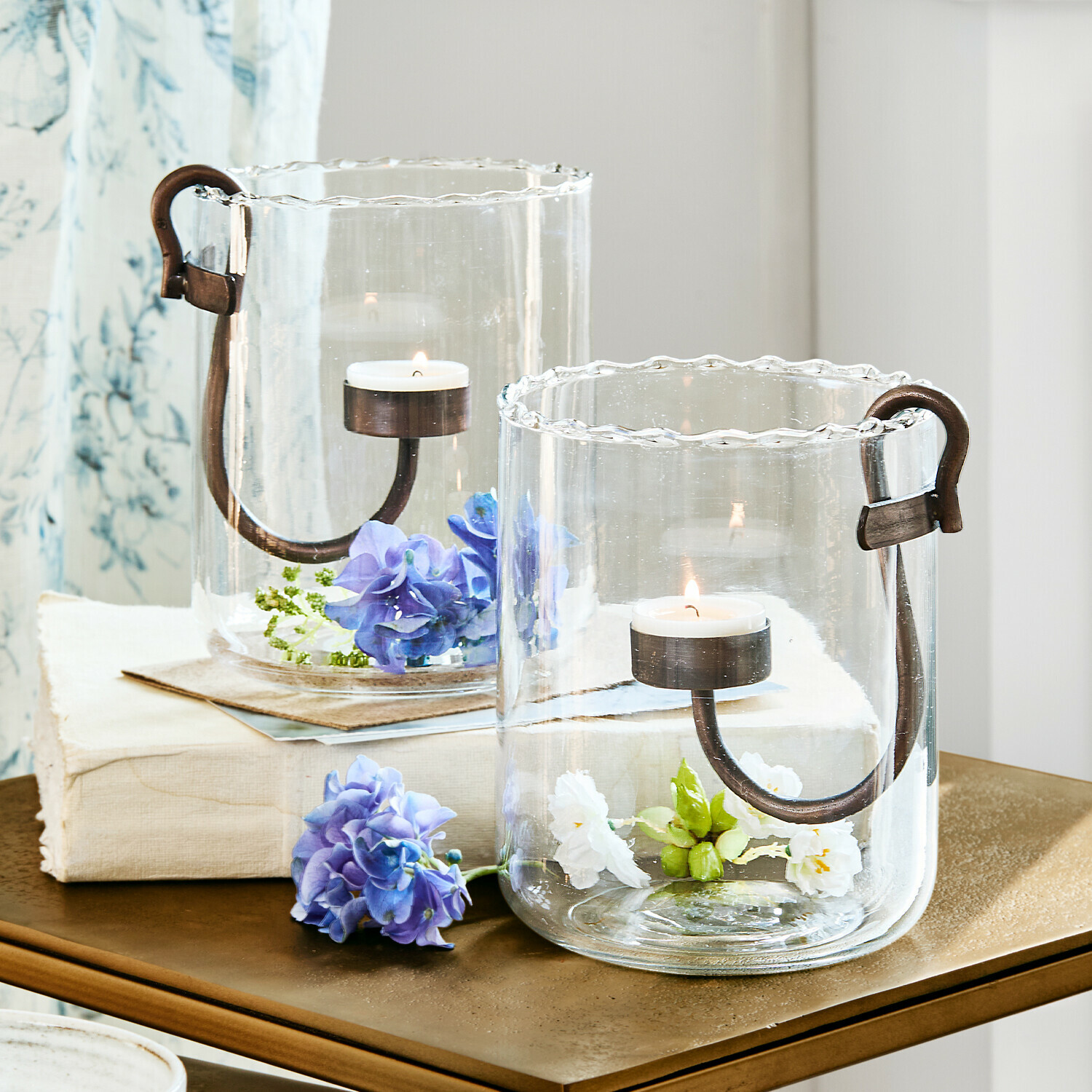 Glazen windlichten met metalen handvatten en bloemen, stijlvolle tafeldecoratie