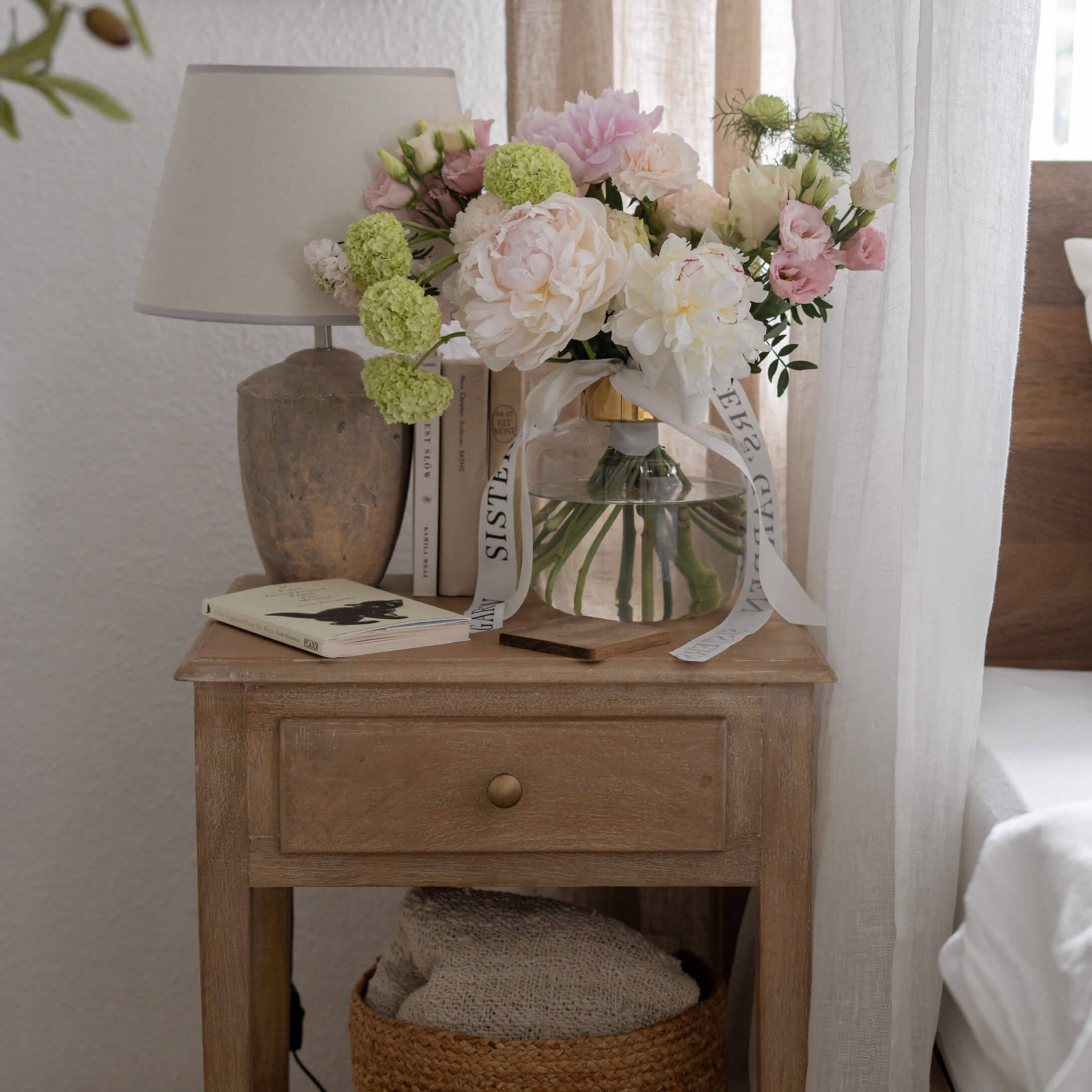 Houten nachtkastje met lade, lamp en vaas met pastelkleurige bloemen in lichte kamer