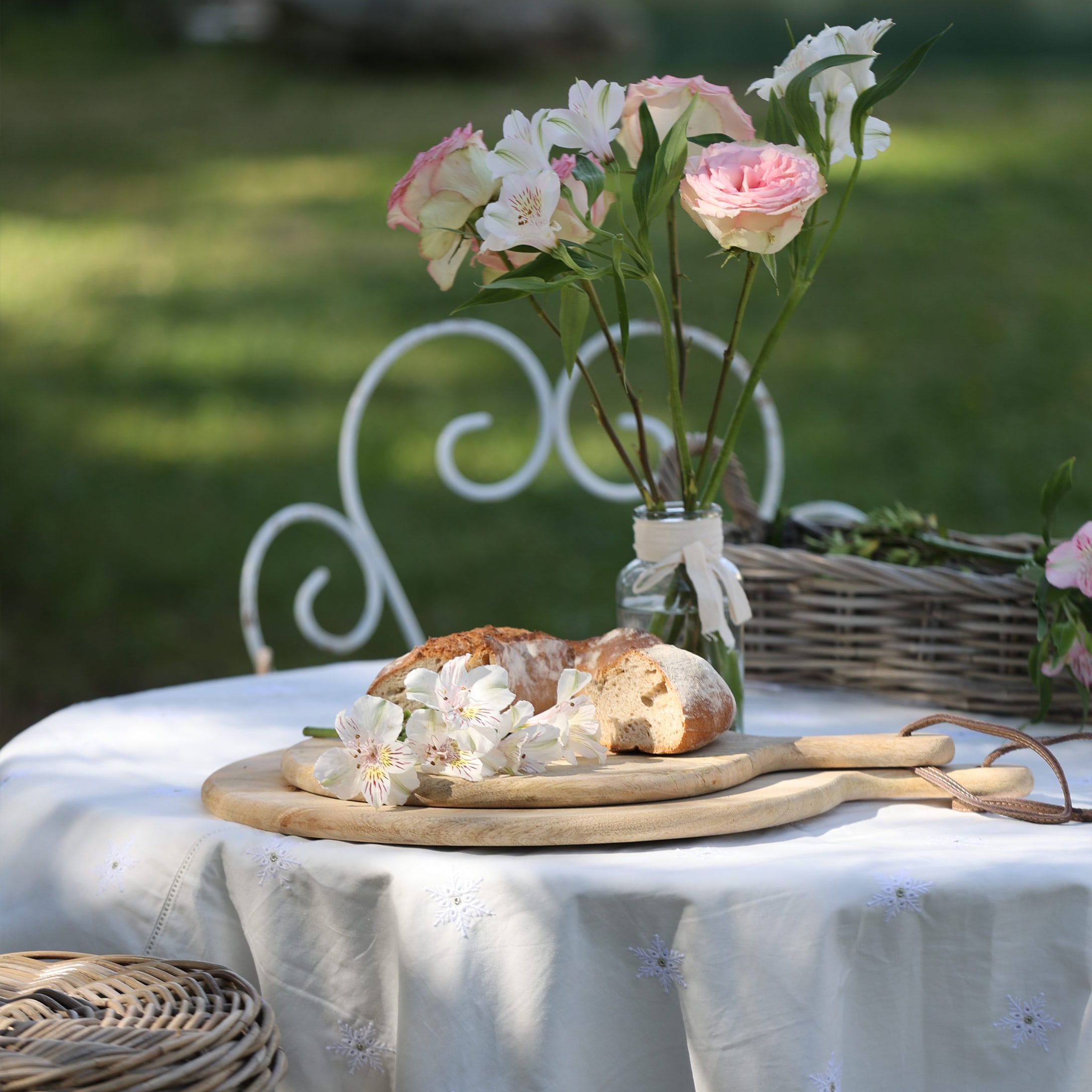 Houten snijplanken op wit tafelkleed met bloemen en brood in de tuin