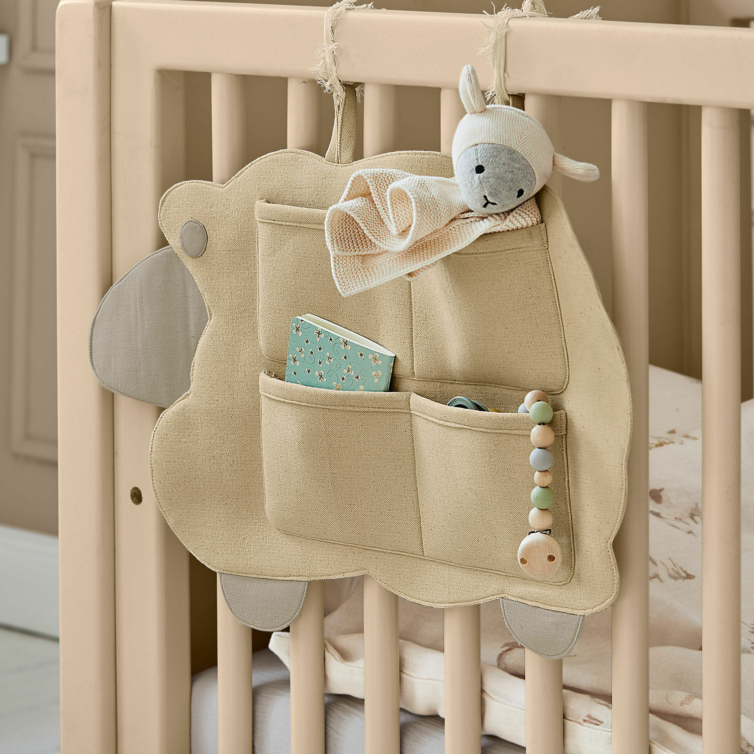 Wandorganizer Erianna Beige katoenen organizer met vakken en schapenknuffel aan een houten babybedje