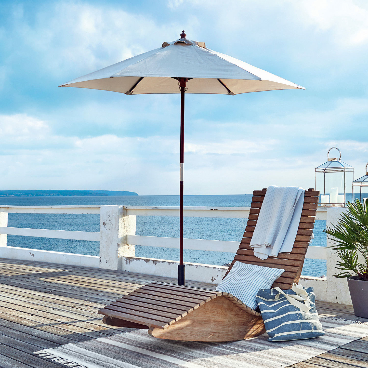 Ligstoel van natuurlijk teakhout met parasol en kussen op terras aan zee