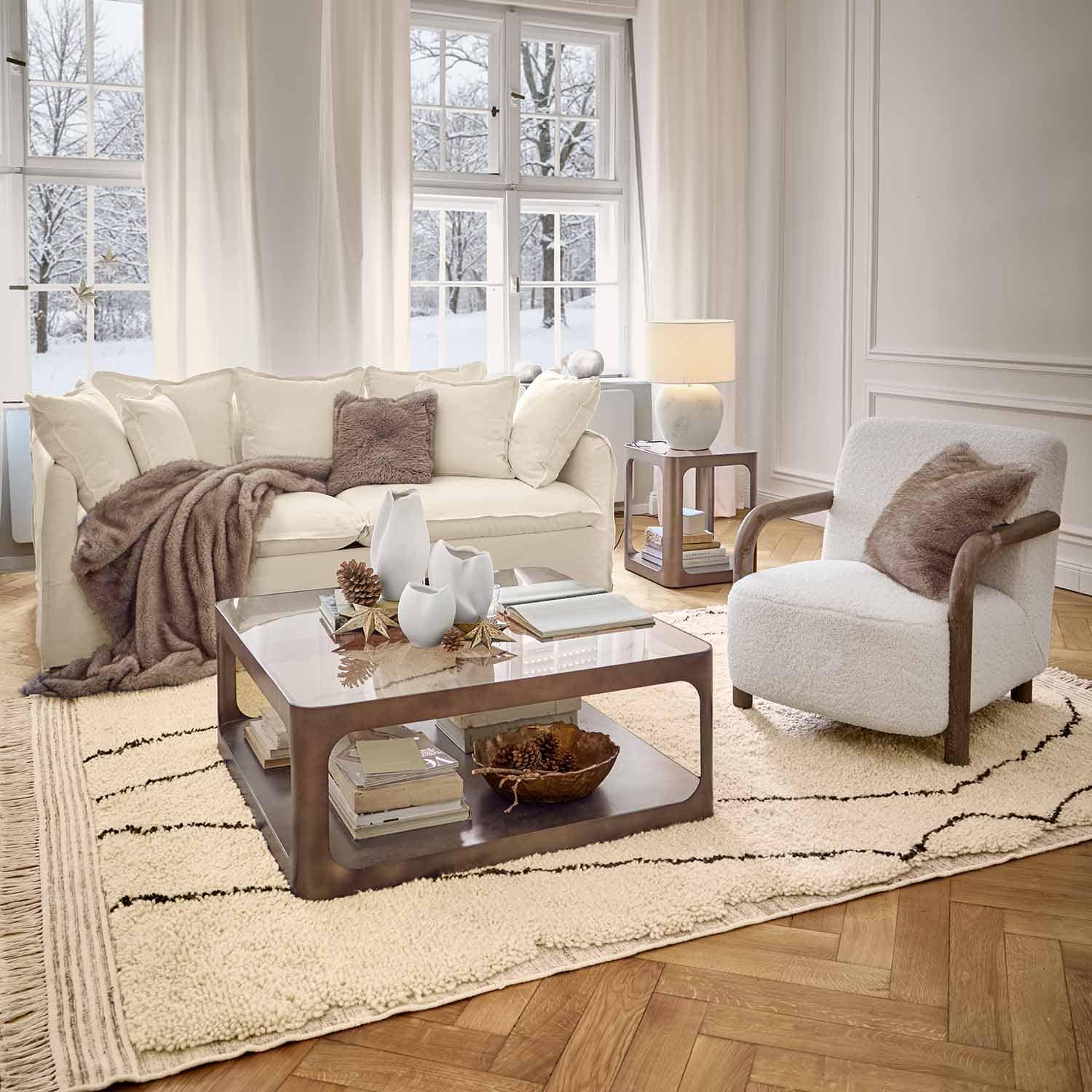 Gezellige woonkamer met witte bank, stoel met houten armleuningen en zachte vloerkleed in winterse sfeer