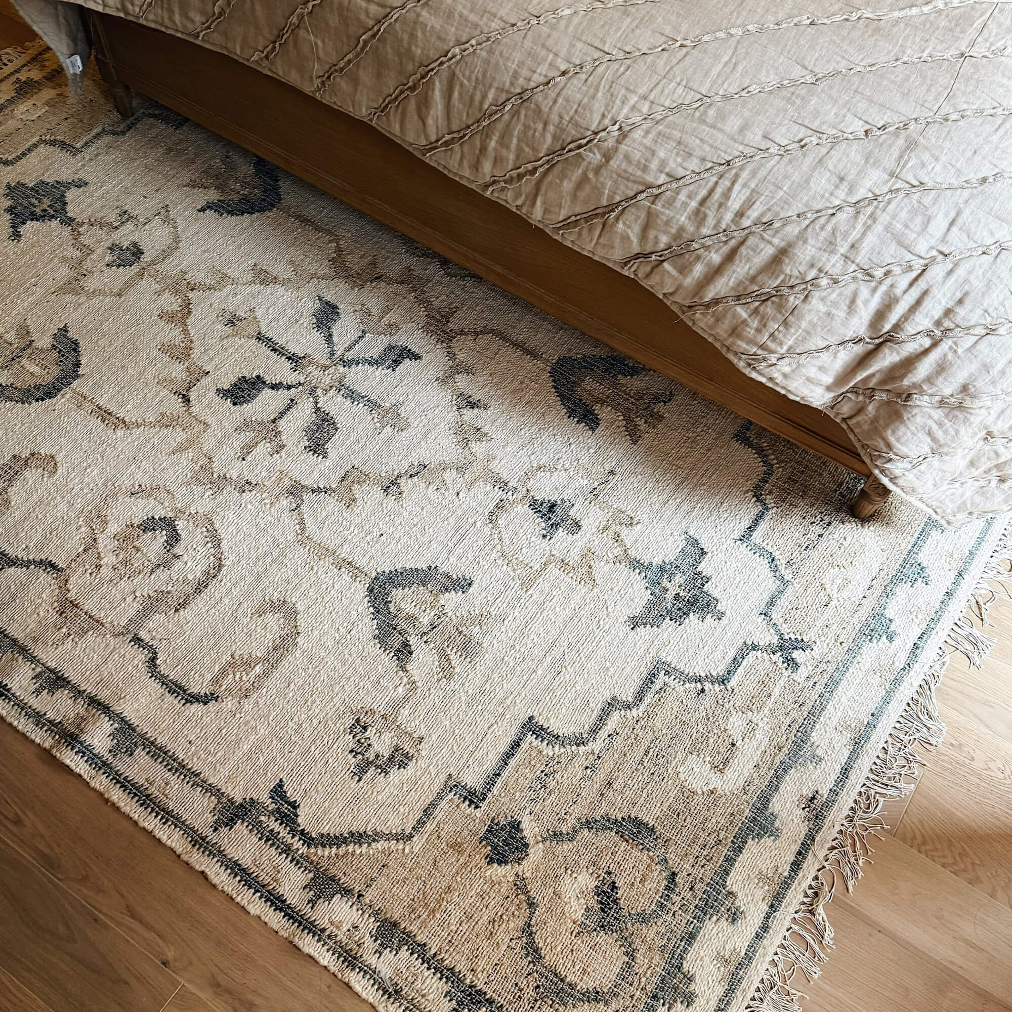 Decoratief beige-grijs vloerkleed onder een houten bed, stijlvolle woonaccessoire