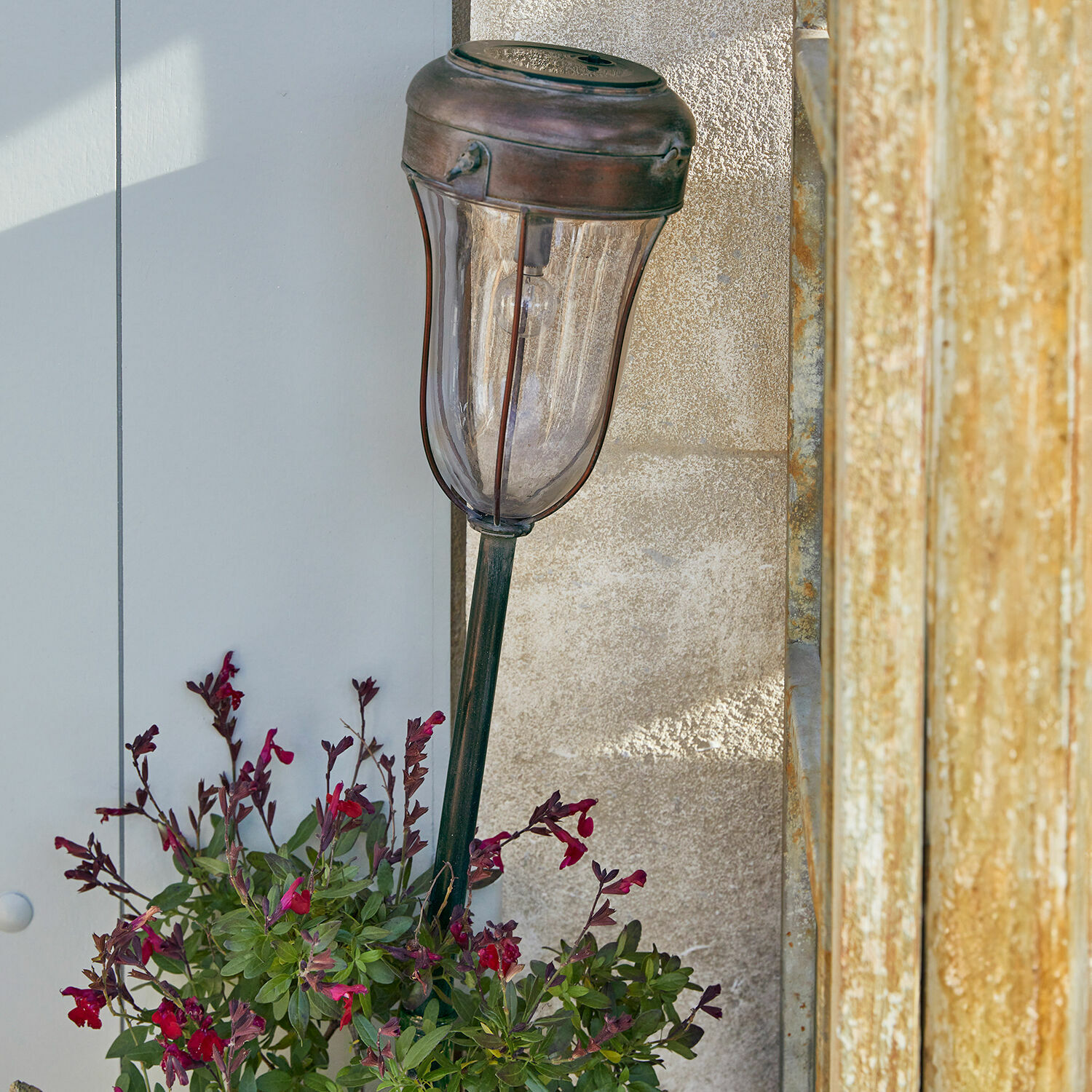 Decoratieve tuinlamp van messing in koperen kleur met doorzichtige kap en rode bloemen