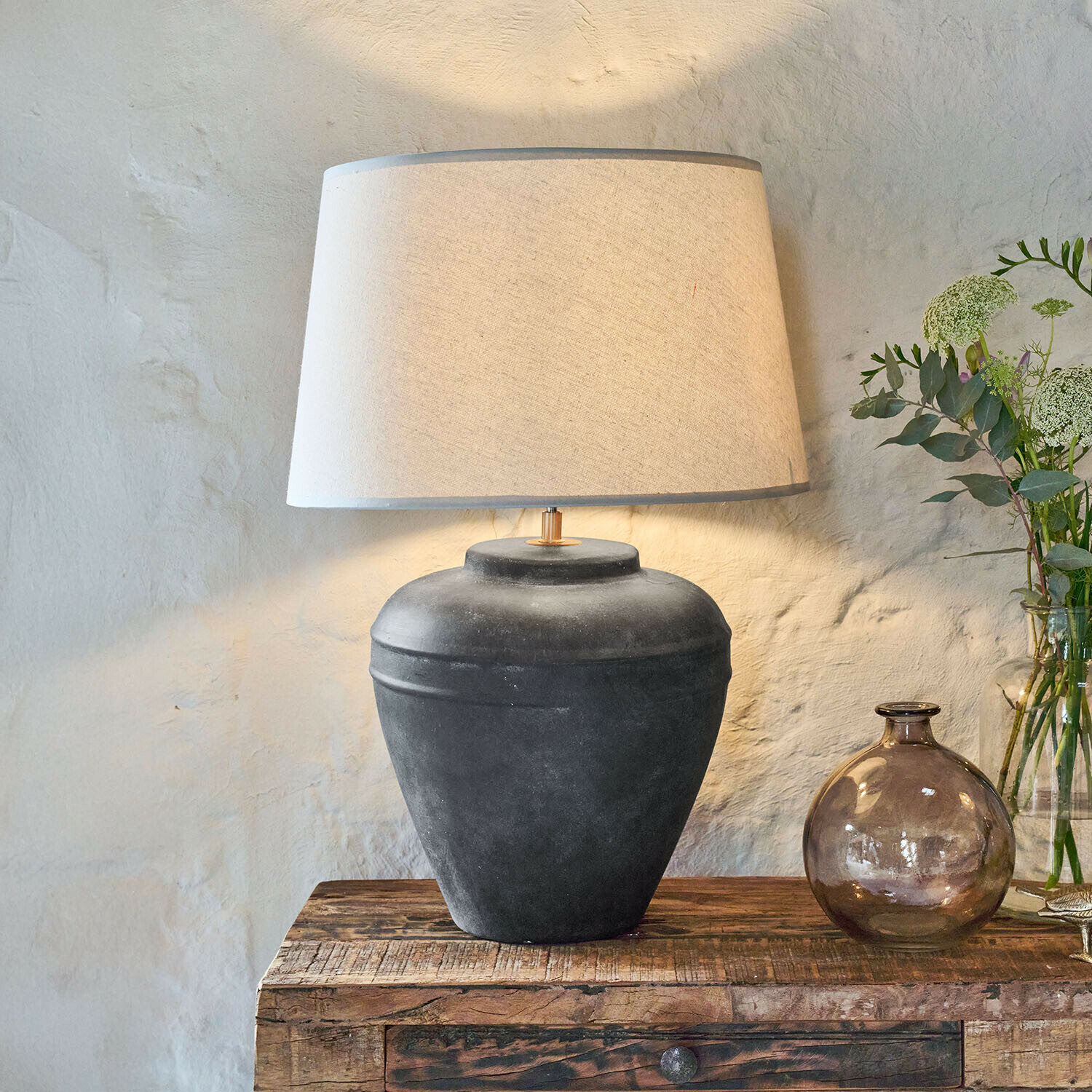 Tafellamp van zwarte keramiek met beige kap op rustieke houten tafel in woonkamer