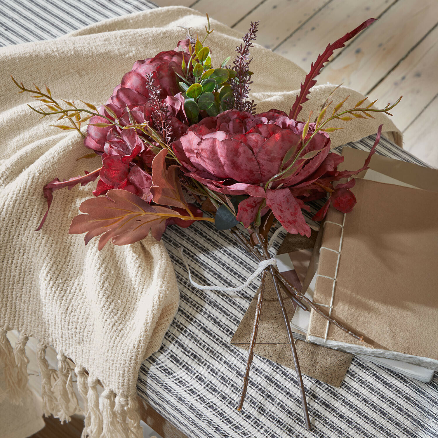 Boeket van kunstmatige rode bloemen met groen blad op een beige plaid en gestreept tafelkleed