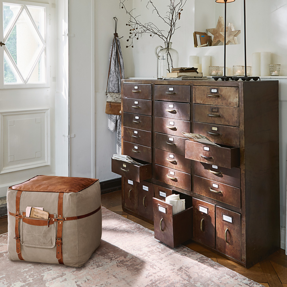 Vintage metalen ladekast met veel lades en beige poef met bruine riemen in lichte kamer