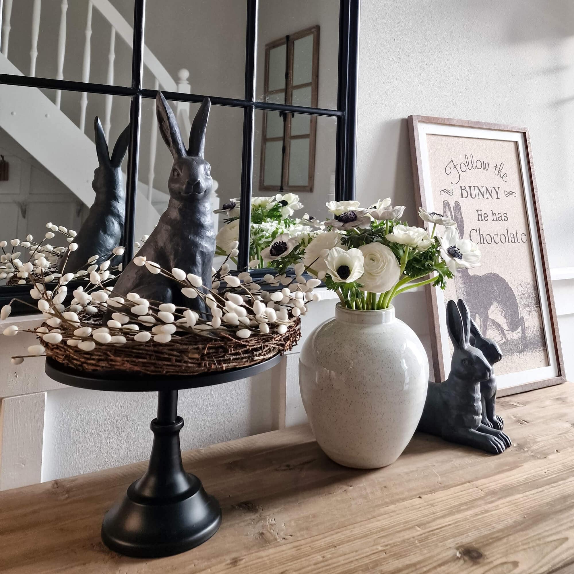 Decoratief zwart konijn met wilgenkrans en witte bloemen in keramische vaas op houten tafel