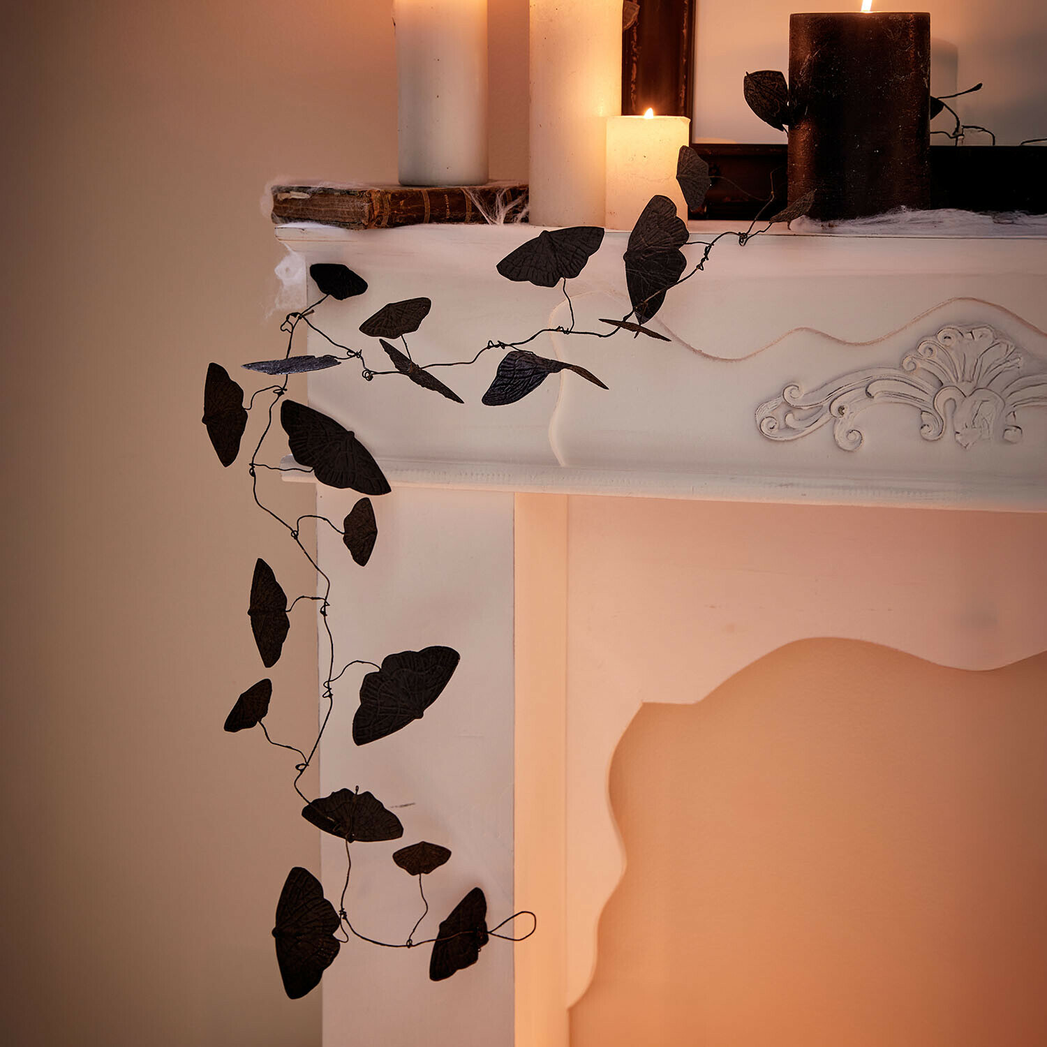 Guirlande Orlenaith Decoratieve zwarte bladrank aan witte open haard met brandende kaarsen