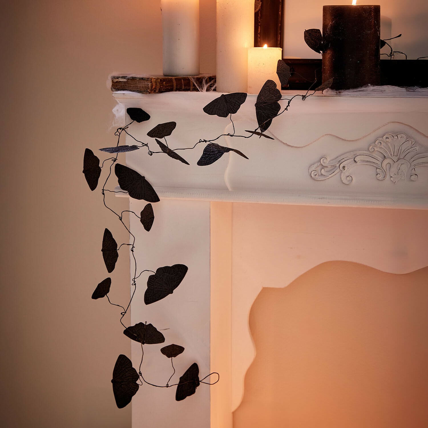 Guirlande Orlenaith Decoratieve zwarte bladrank aan witte open haard met brandende kaarsen