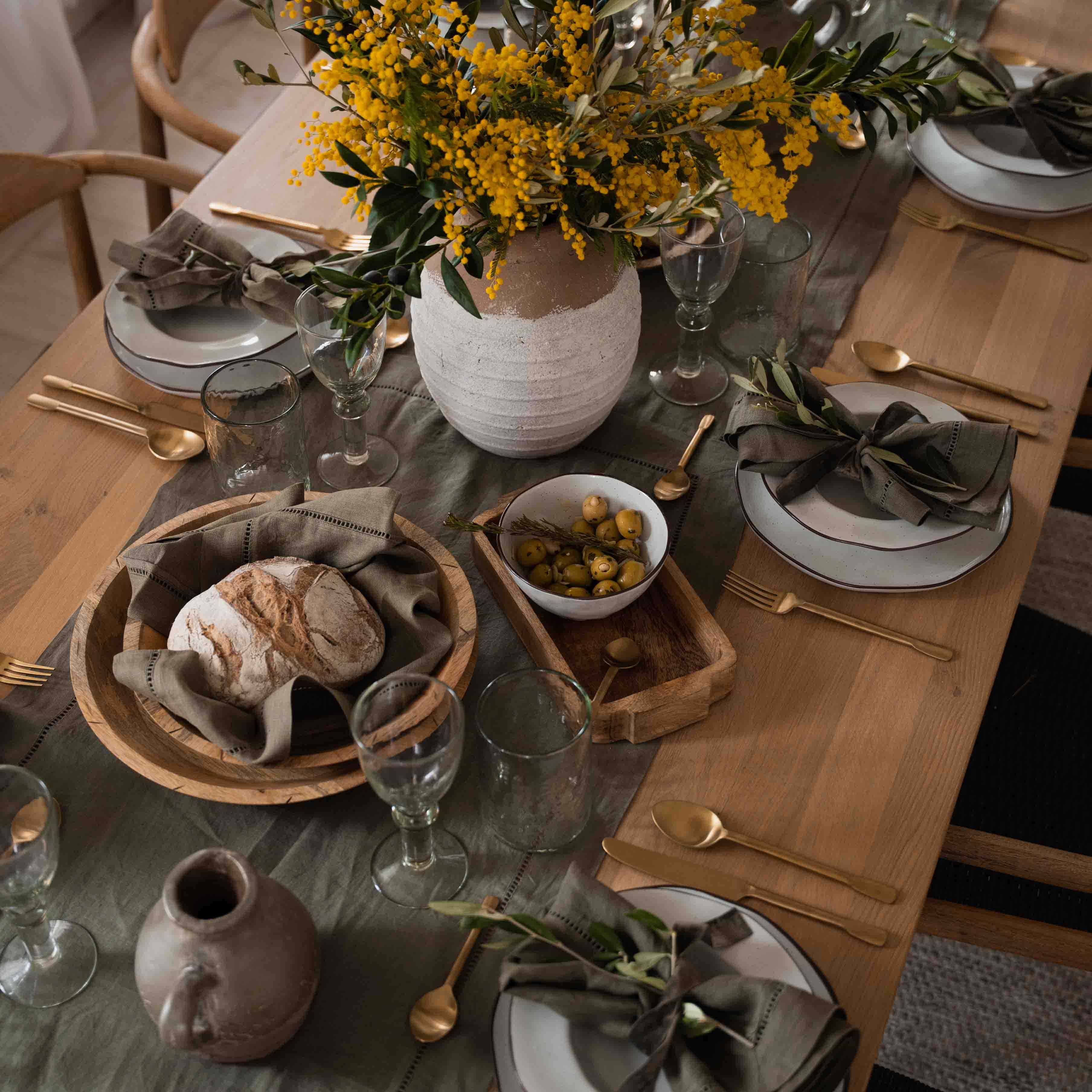 Rustieke houten tafel met wit servies, groene servetten en gele bloemen in een aardewerken vaas
