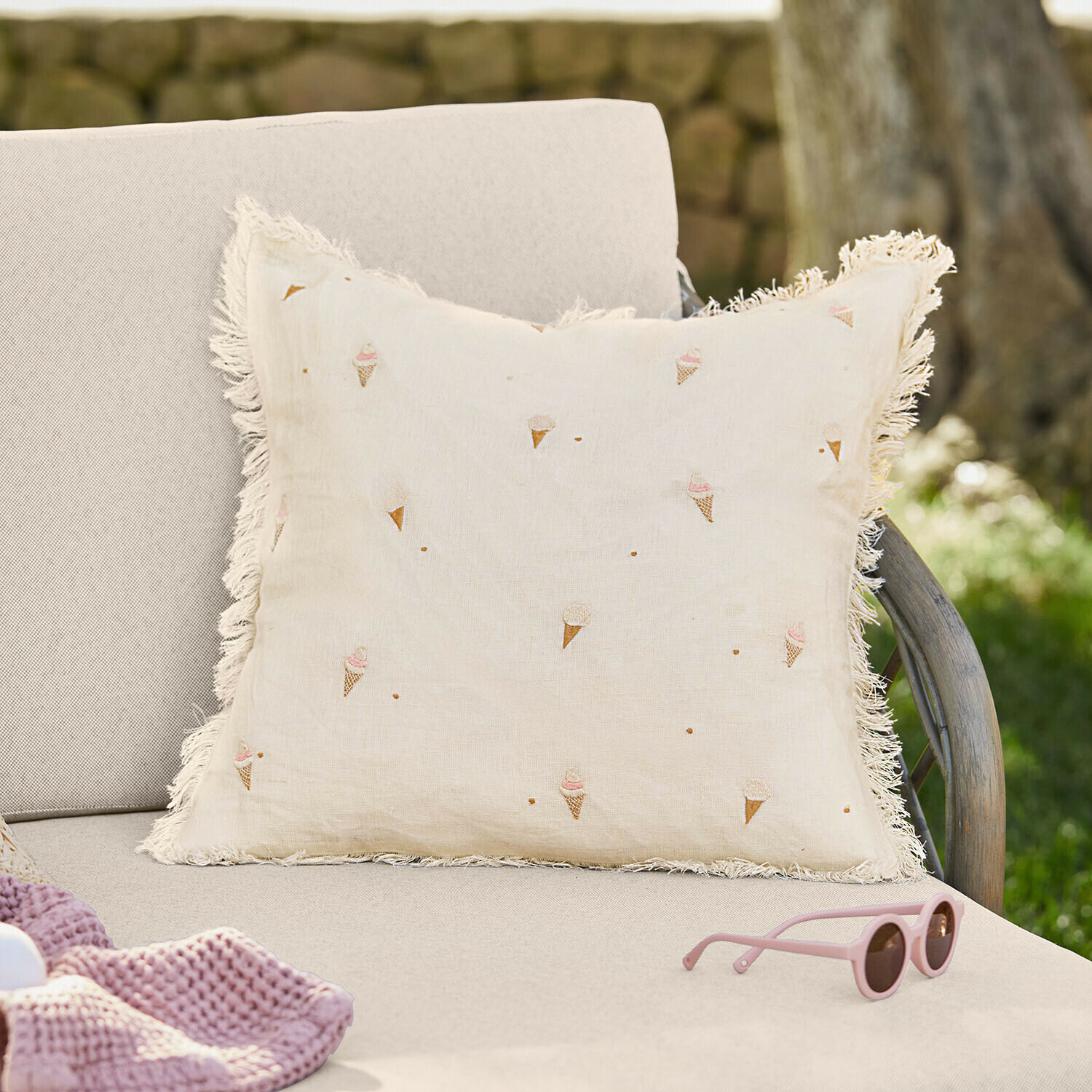 Beige linnen kussen met franjes en ijsjespatroon op lichte bank in de tuin
