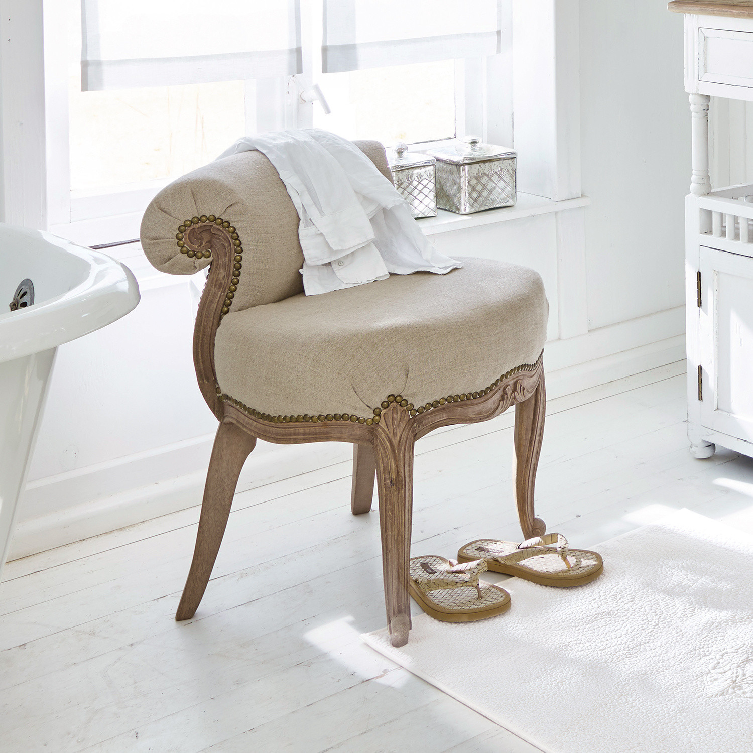 Beige gestoffeerde stoel met gesneden houten frame in lichte badkamer