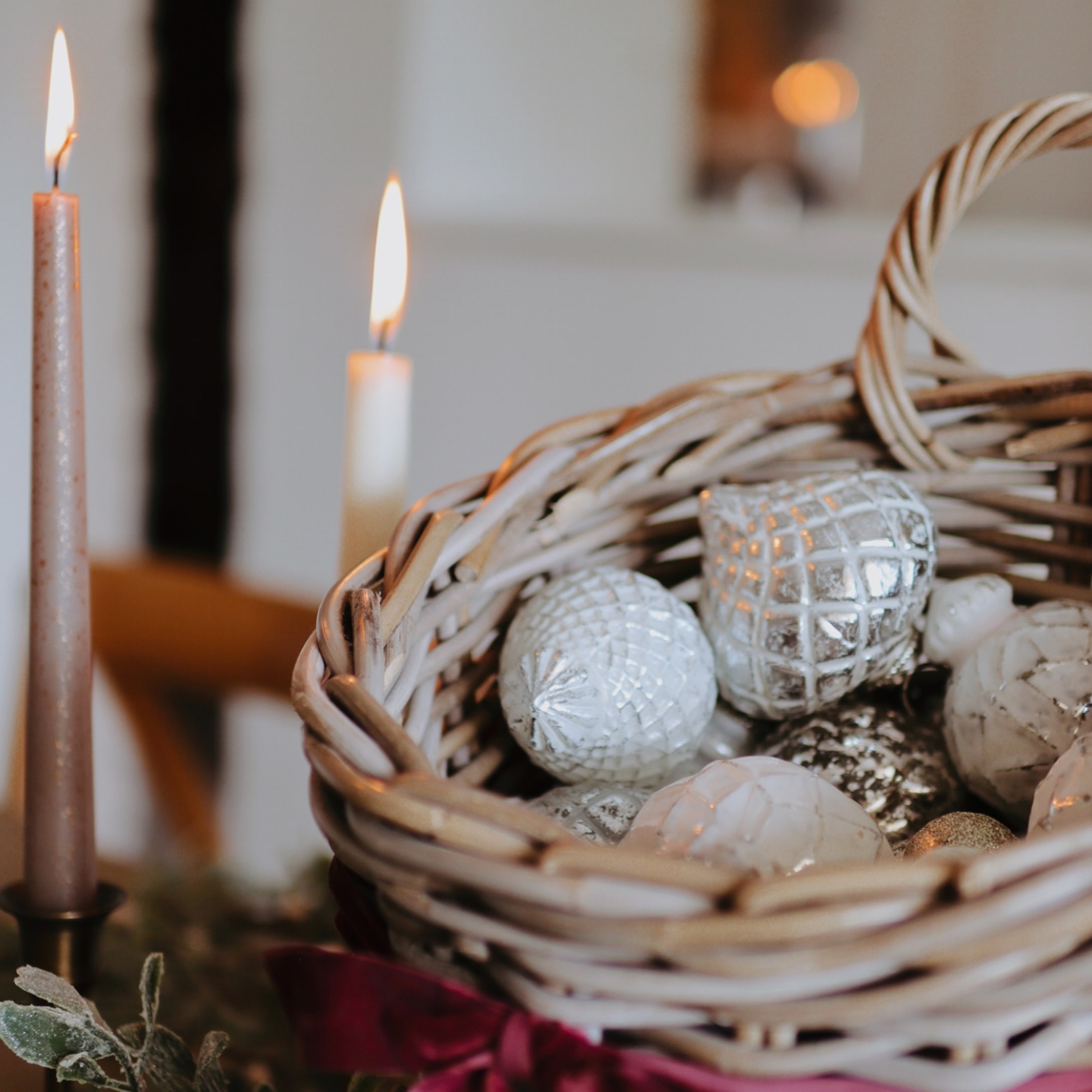 Rieten mand met zilveren en witte kerstversieringen, brandende kaarsen op de achtergrond