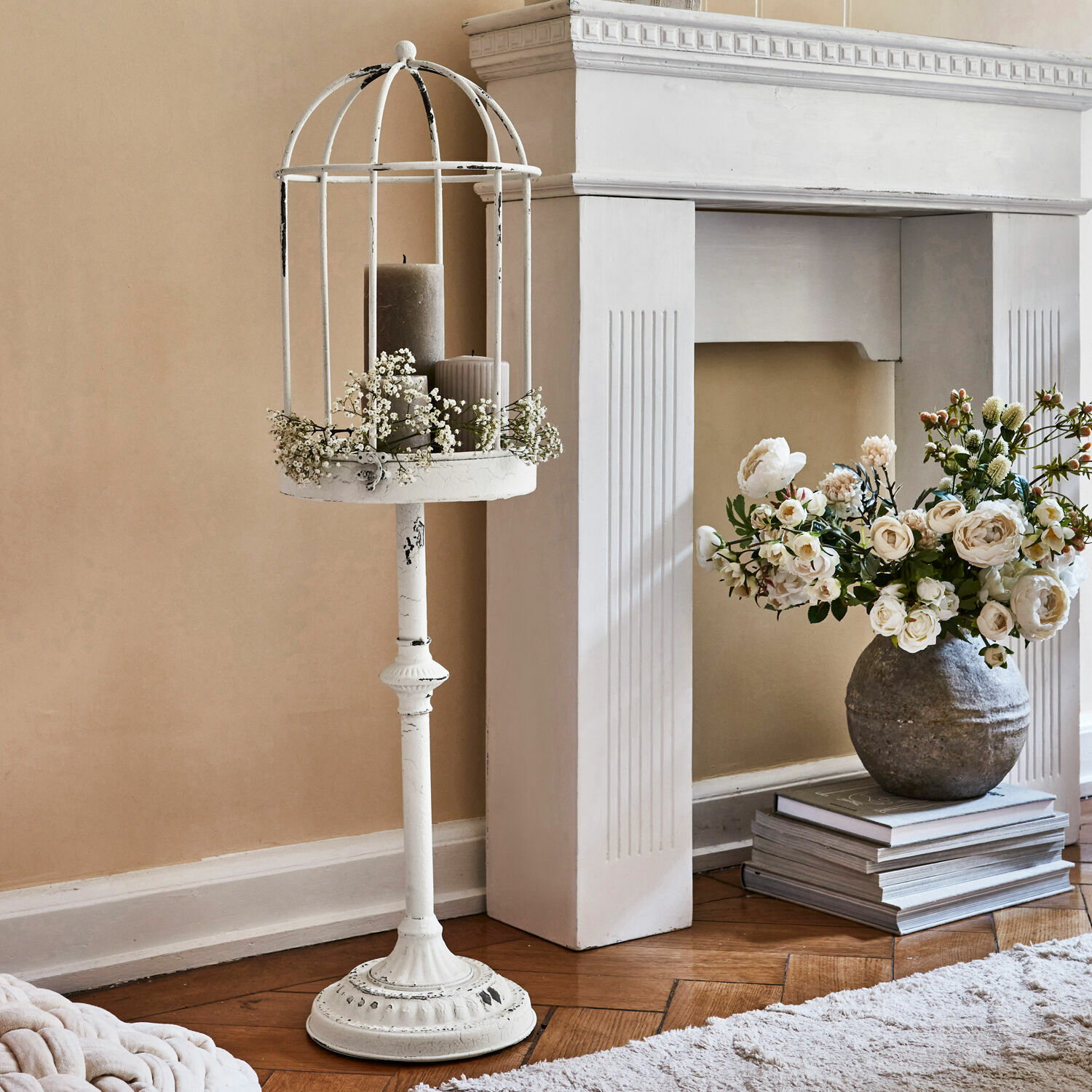 Witte metalen staande kandelaar met decoratieve kooi en grijze kaarsen in vintage stijl