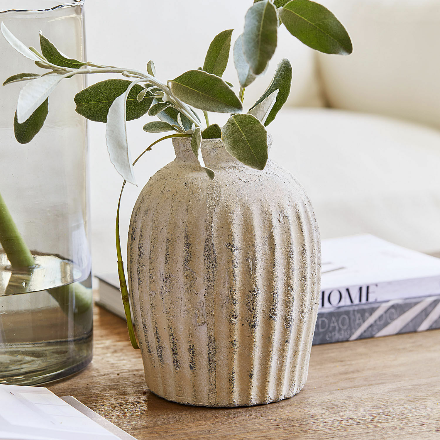 Beige keramische vaas met structuur en groene bladeren op houten tafel voor interieurdecoratie