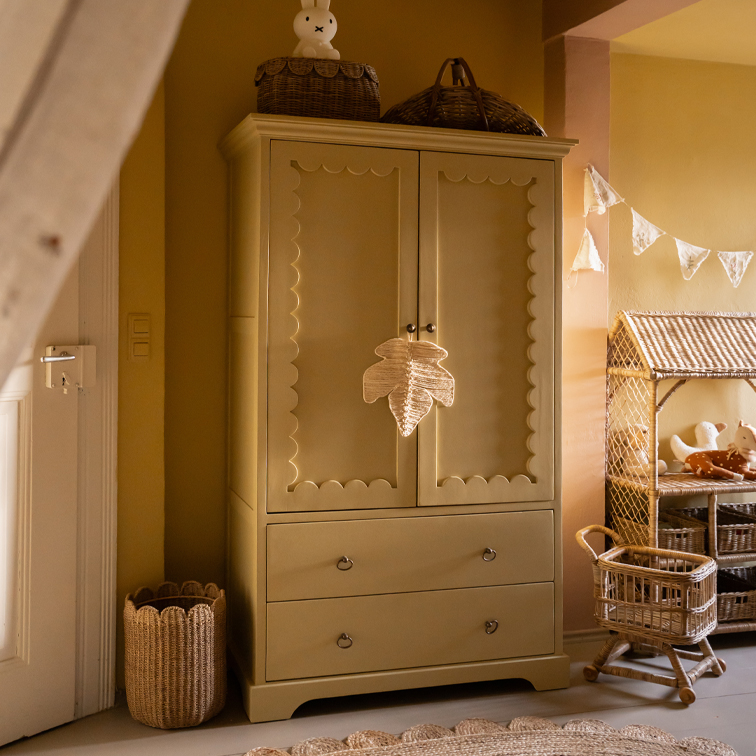 Beige houten kast met decoratieve panelen en twee lades in een gezellige kinderkamer