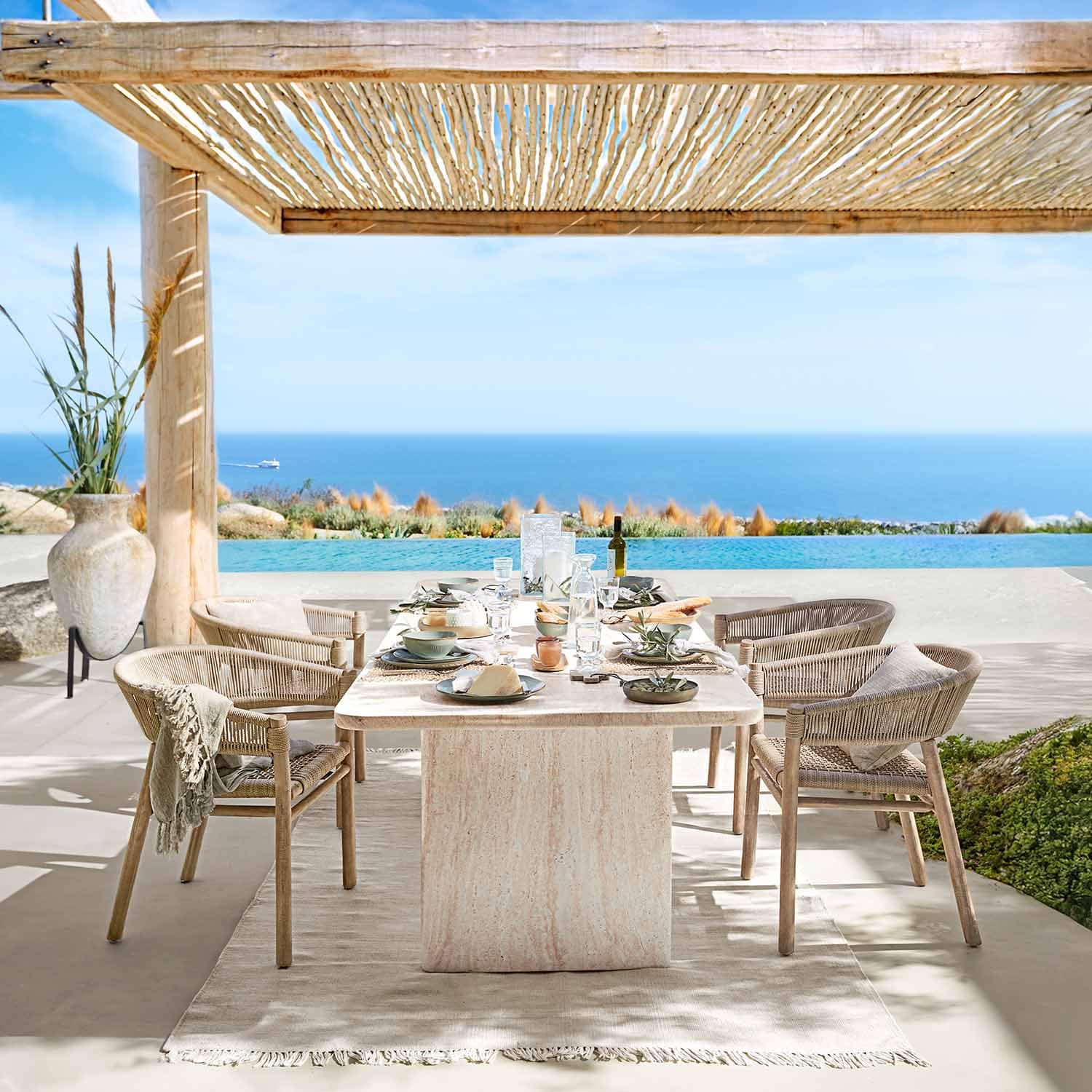 Buiteneetruimte met natuurstenen tafel en rotan stoelen met uitzicht op zee