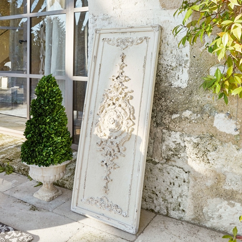 Wit decoratief houten paneel met vintage reliëf tegen een stenen muur naast een groene plant
