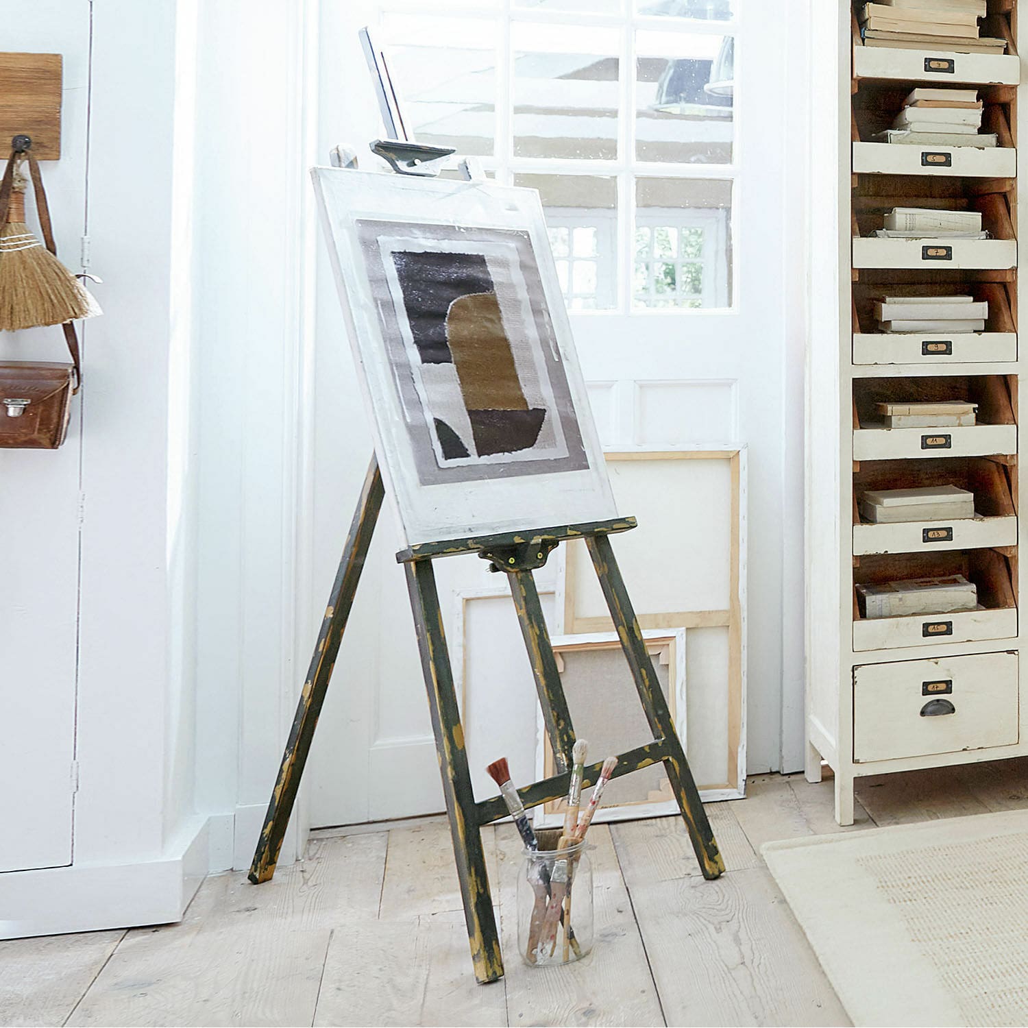 Schildersezel Arabella Vintage houten schildersezel met schilderij en penselen op lichte vloer in atelier