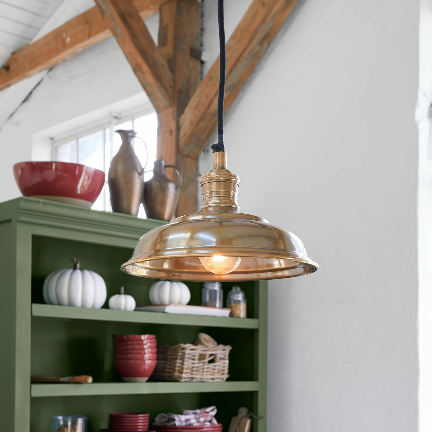 Messing hanglamp met zwarte kabel in rustieke keuken met groene kast en decoraties