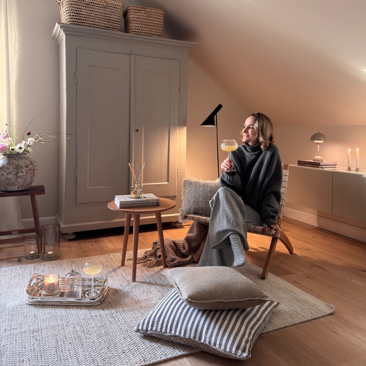Gezellige zithoek met houten stoel, grijze deken en kaarsen op lichte vloerkleed