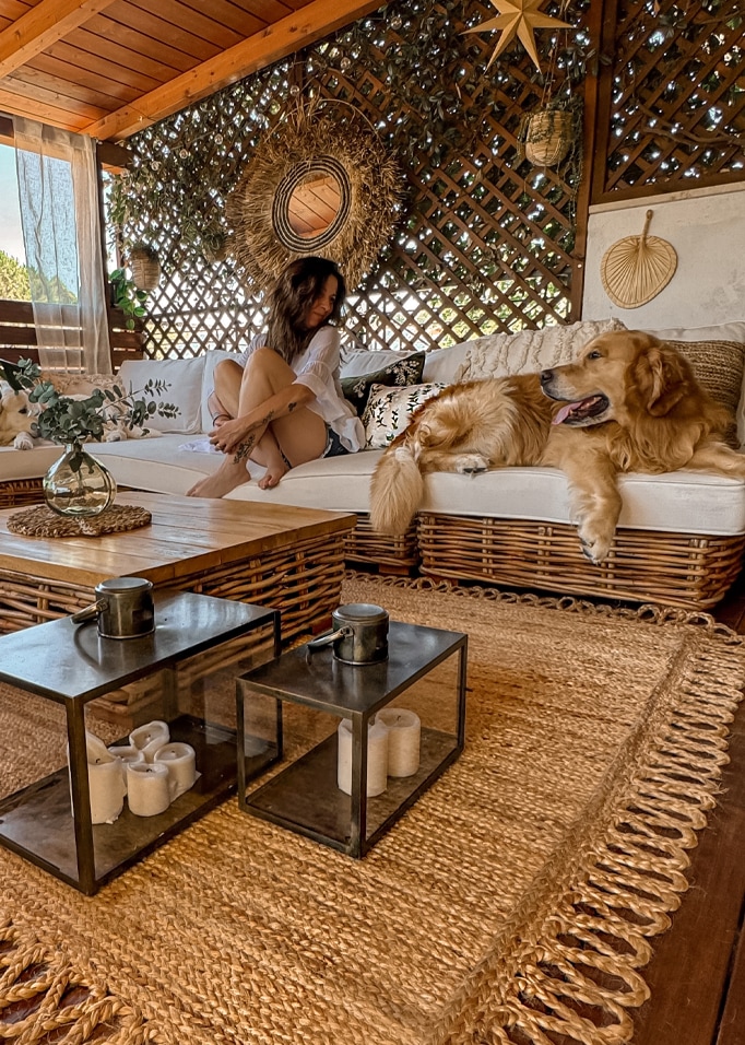 Gezellige woonkamer met rotan bank, natuurlijke jute vloerkleed, boho decoraties en hond op de bank