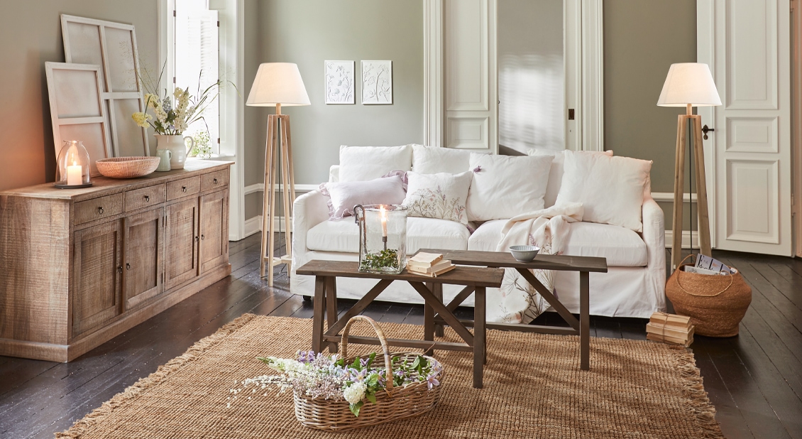 Gezellige woonkamer met witte bank, houten tafel en natuurlijke jute vloerkleed, bloemrijke decoratie