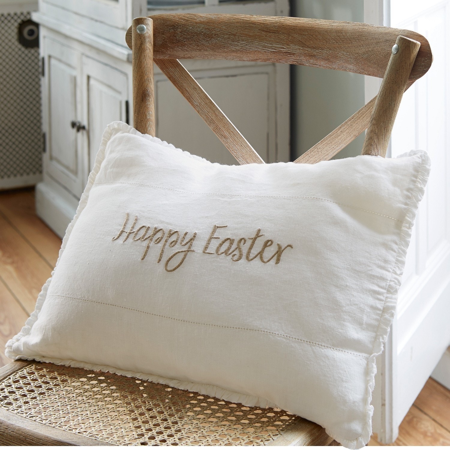 Witte linnen sierkussen met Happy Easter borduurwerk op houten stoel, paasdecoratie