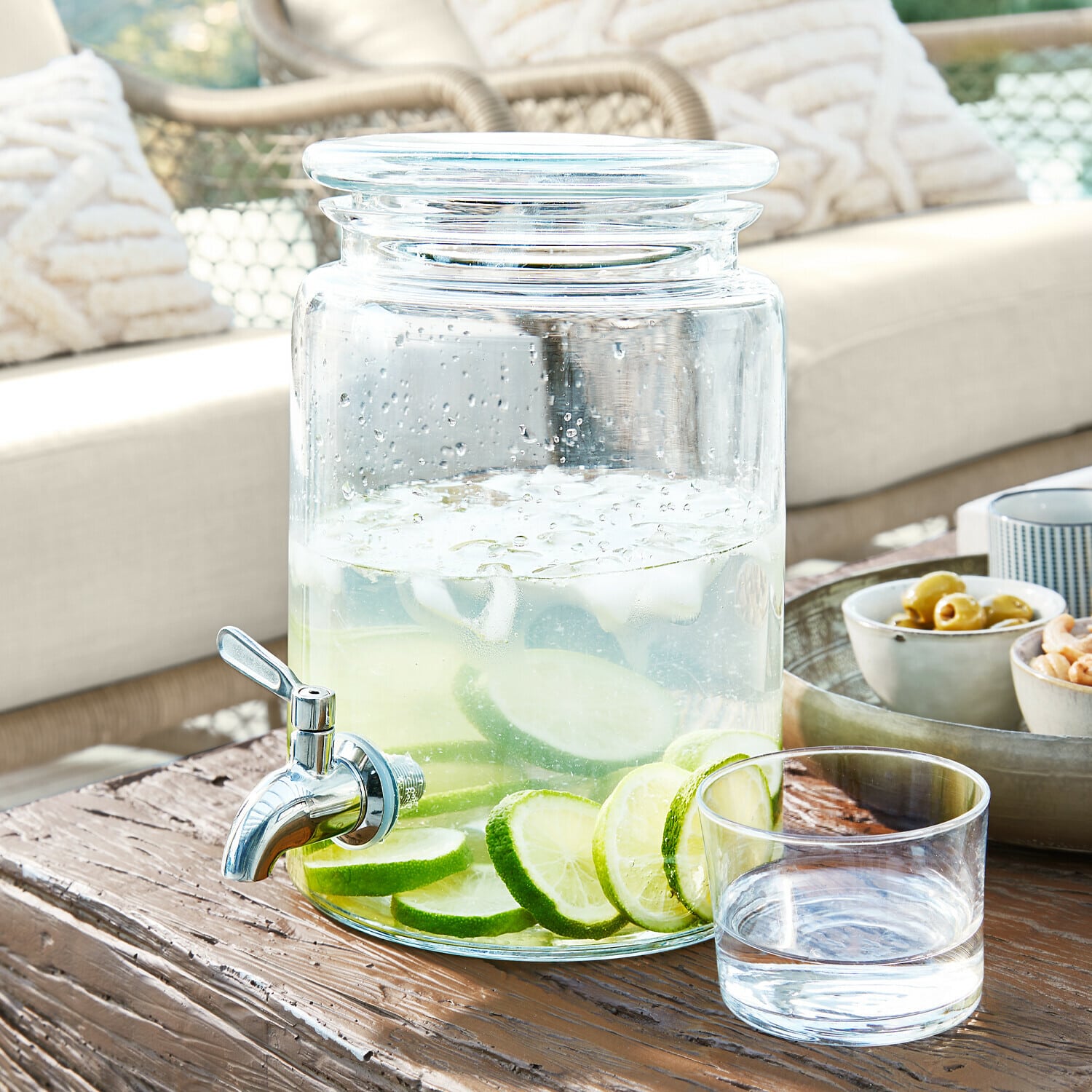 Glazen drankendispenser met kraan, gevuld met water en limoenplakjes op houten tafel
