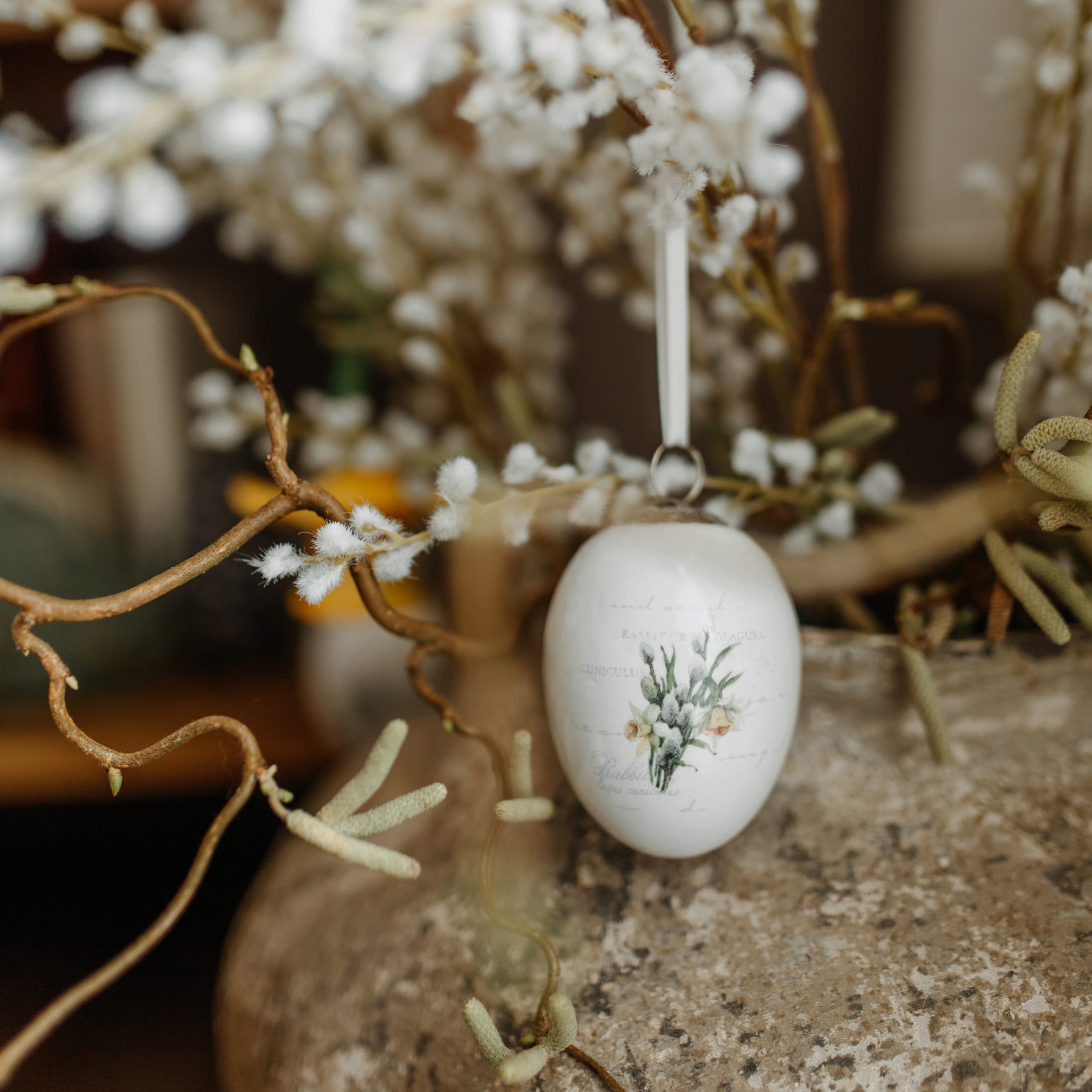 Witte keramische paasdecoratie in de vorm van een ei met bloemenmotief aan een decoratieve tak