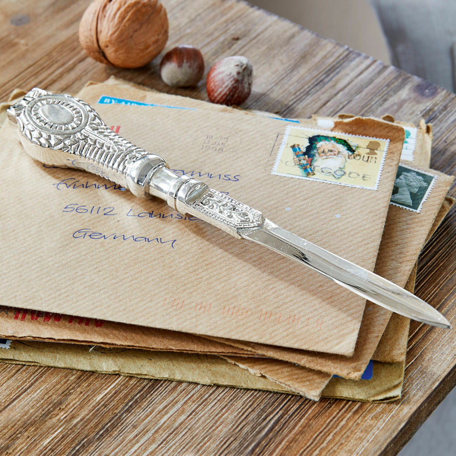 Briefopener Parsifal Zilverkleurig versierd briefmes op enveloppen met noten op houten tafel