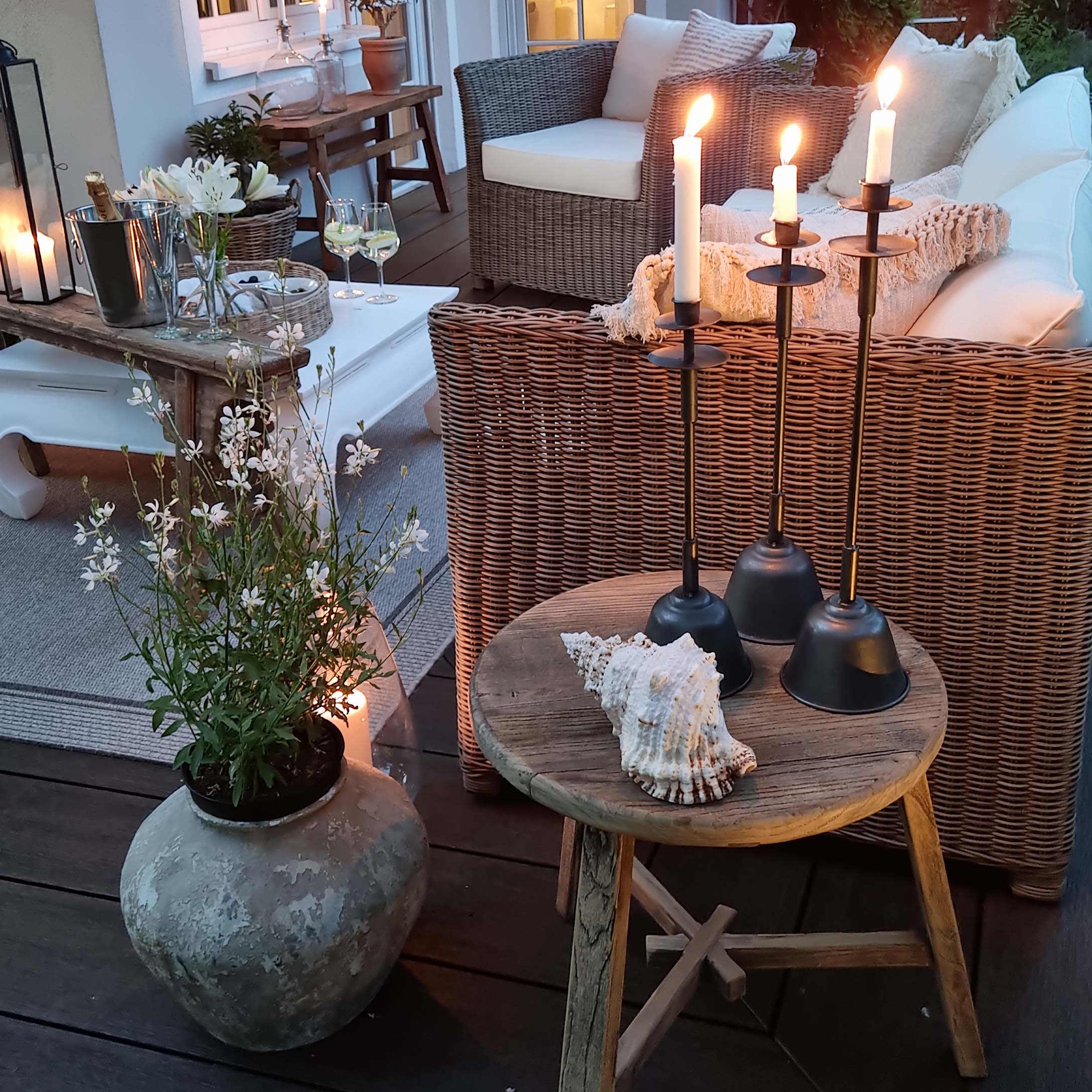 Gezellig terras met rotan bank, houten tafel en metalen kandelaren met witte kaarsen