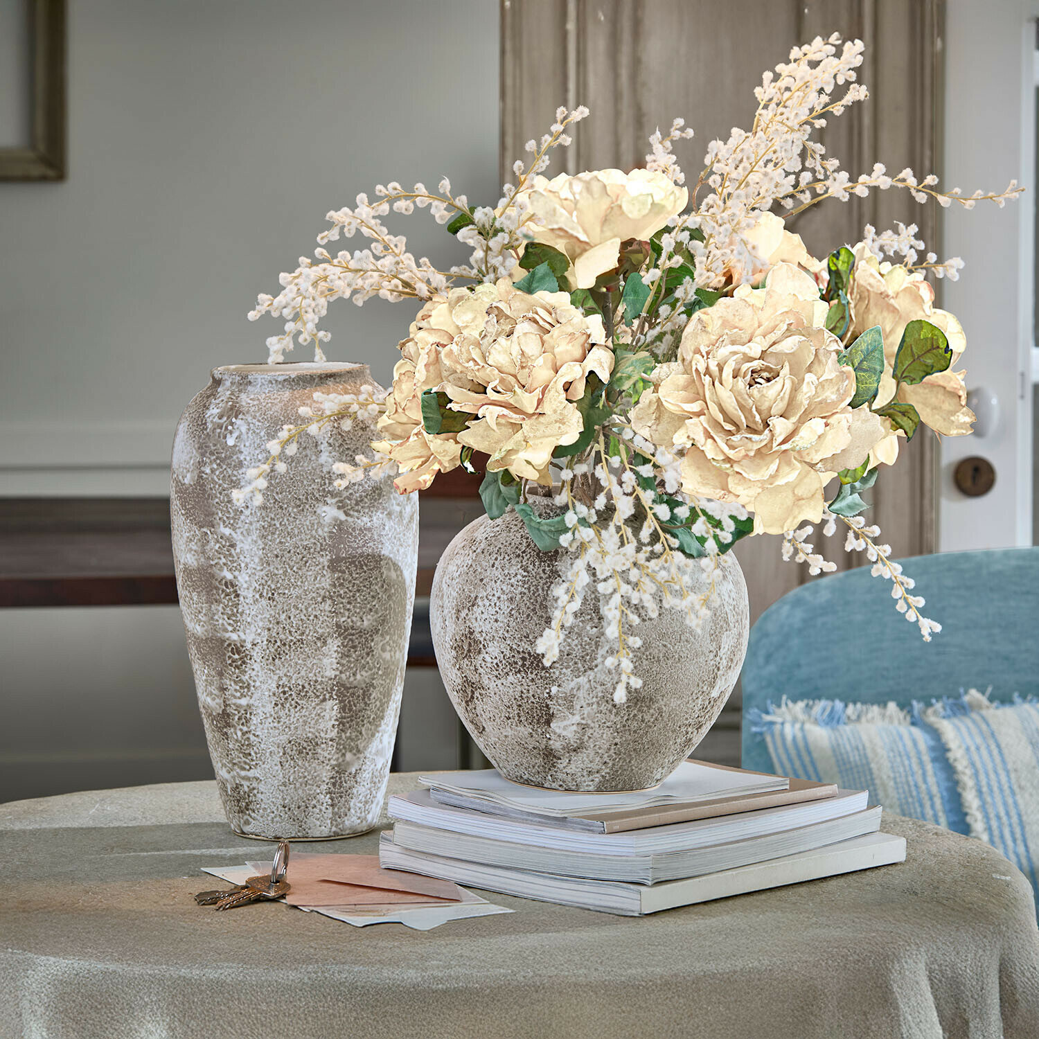 Decoratieve keramische vaas in beige-bruin met crèmekleurig boeket op tafel met gestapelde boeken
