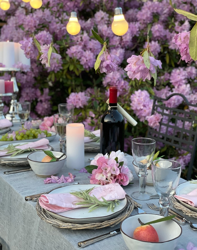 Zomerse tafeldecoratie met roze bloemen, lichtsnoer en wijnfles voor paarse struiken.