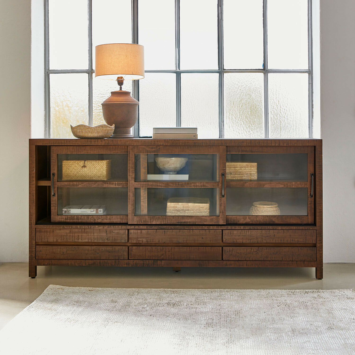 Houten dressoir met glazen deuren en lades, gedecoreerd met lamp en gevlochten manden