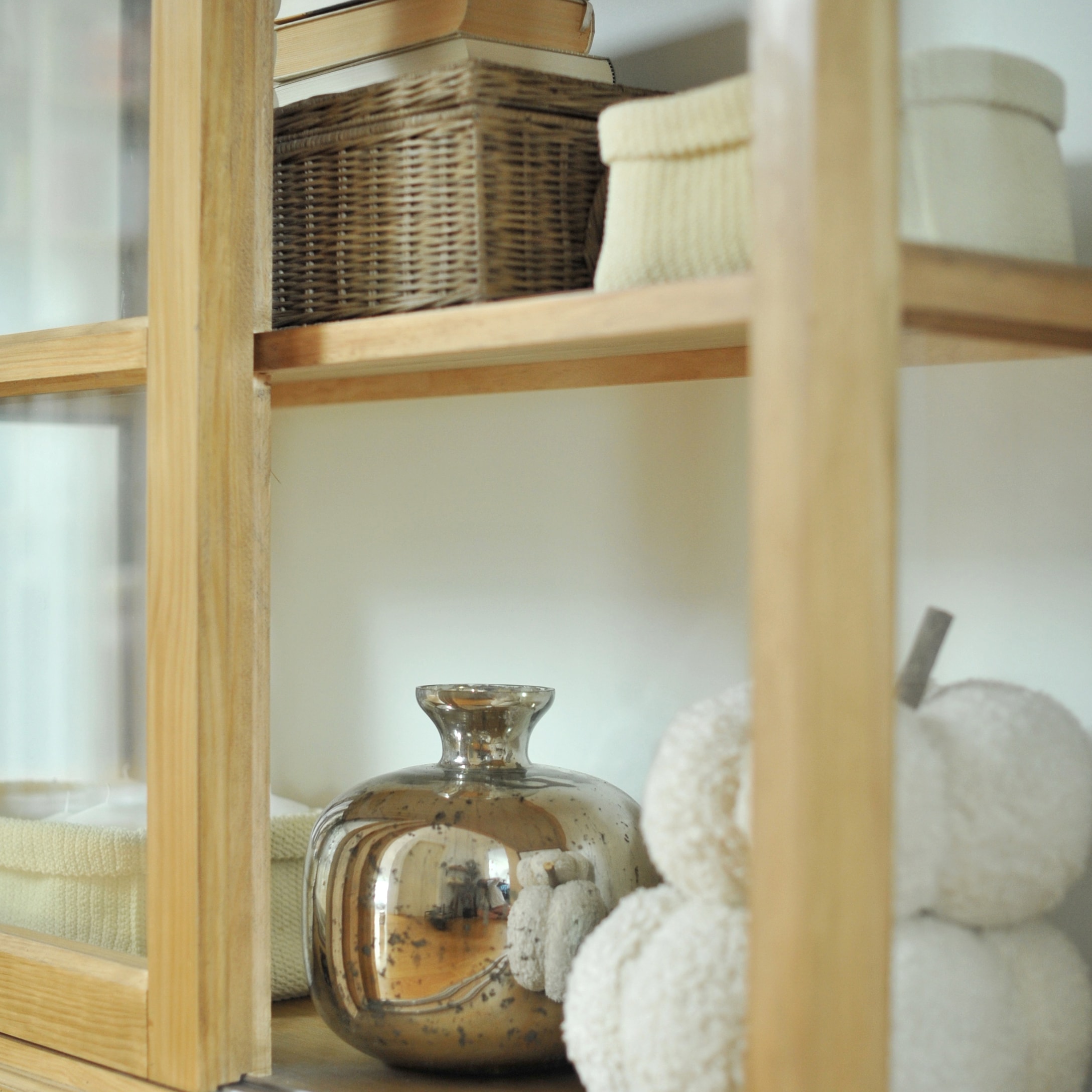 Decoratieve zilveren glazen vaas op houten plank met rieten mand en crèmekleurige decoraties