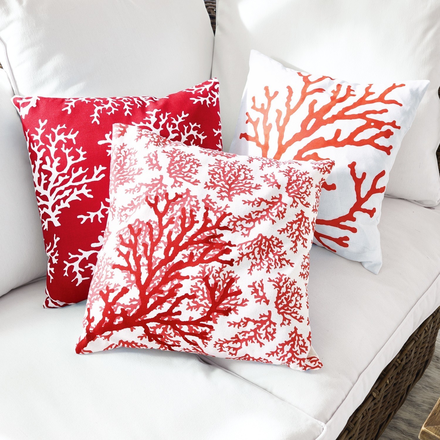 Drie decoratieve kussens met rood koraalpatroon op witte stof op een lichte bank