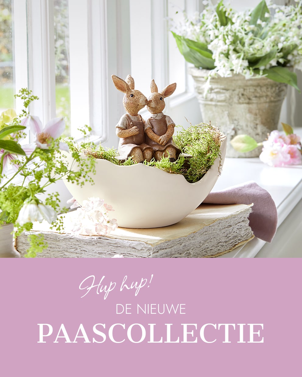 Twee konijnenfiguren in een beige schaal met mos, omringd door lentebloemen en decoratie